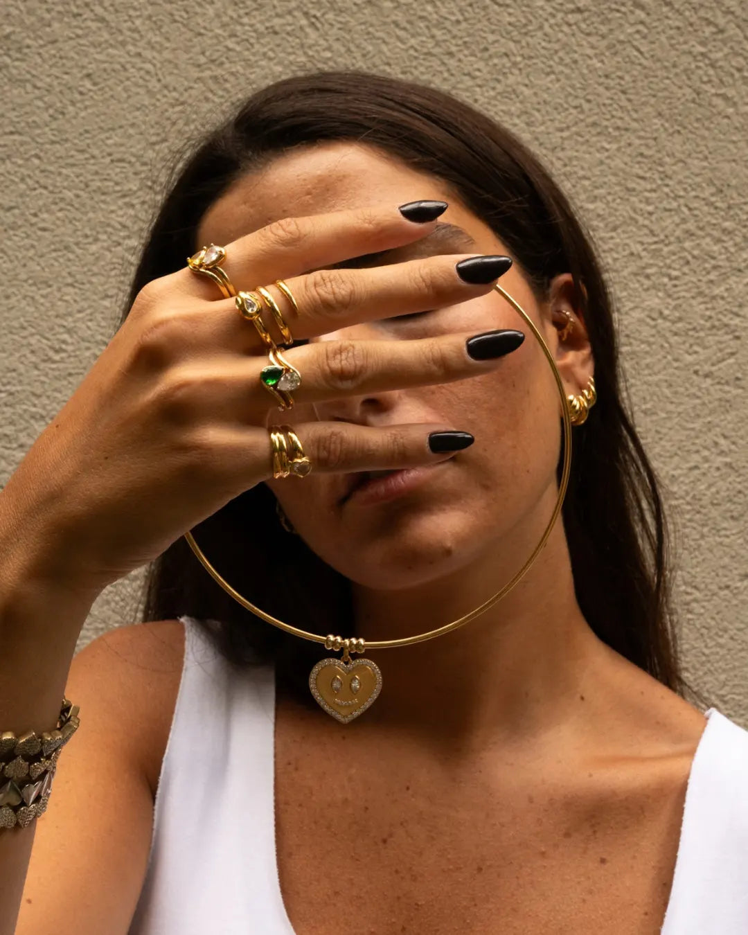 collection de bagues en plaqué or portés sur une main, avec des zirconiums et un collier torque en plaqué or avec un pendentif en forme de coeur.